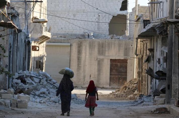 Civilians walk past damaged buildings in the rebel-held al-Sheikh Said neighbourhood of Aleppo